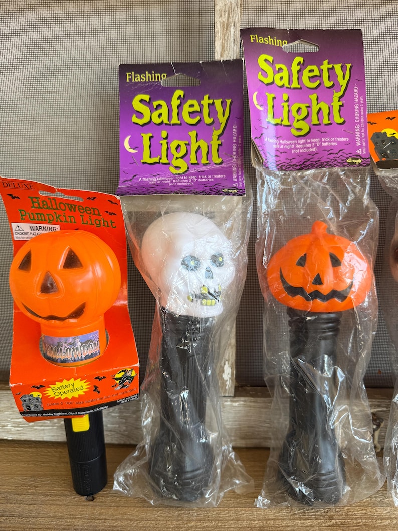 May include: A collection of Halloween-themed flashing safety lights. The lights include a pumpkin, a skull, and a pumpkin-shaped light. The packaging features the words "Flashing Safety Light" and "Halloween Pumpkin Light".