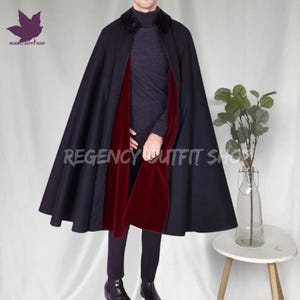 May include: A black cape with a velvet collar and a deep red lining. The cape is open in the front, revealing the red interior. The text "REGENCY OUTFIT SHOP" is visible on the cape. A stylish outerwear garment.