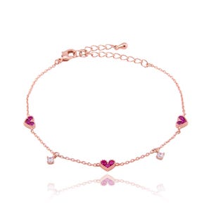 Puede incluir: Un delicado tobillo de oro rosa con tres dijes de corazón rosa y dos pequeños dijes de cristal transparente.