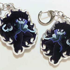 May include: Two clear acrylic keyrings featuring a stylized anime character with long black hair, a mask, and a dark outfit with purple accents. Each keyring has a silver-coloured clasp.