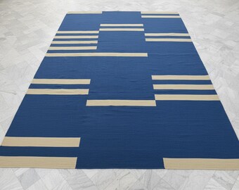 May include: A rectangular blue rug with a geometric design. The rug features horizontal and vertical beige stripes against a solid blue background. The rug is made of a woven material and is suitable for indoor use.