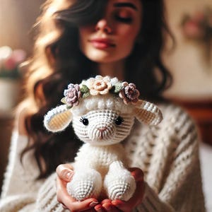 Puede incluir: Un cordero de crochet blanco con una corona de flores hecha de tela rosa, blanca y verde. El cordero está siendo sostenido por una persona.