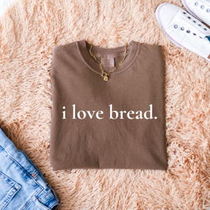 Simple. Honest. Relatable.
This “I Love Bread” Comfort Colors t-shirt is made for anyone who believes bread deserves more appreciation. Featuring clean, minimalist text and a soft, lived-in feel, this tee is the perfect blend of humor and everyday comfort.