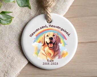 May include: A round white ceramic ornament featuring a colorful rainbow and a golden retriever dog illustration. The text reads Heaven sent, Heaven gained. with the name Rylie and the years 2015-2025 printed below the dog. A jute rope is attached.