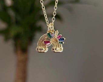 May include: A gold-toned necklace featuring a pendant shaped like a rainbow. The pendant is decorated with small, rectangular, multi-colored gemstones in shades of red, green, blue, purple, and clear, set along the arch of the rainbow design.