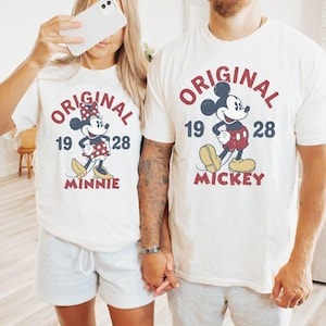 May include: Off-white t-shirts with matching gray shorts. Each shirt features a vintage-style graphic of Mickey and Minnie Mouse with the text "ORIGINAL 1928". The Mickey shirt says "MICKEY" and the Minnie shirt says "MINNIE".