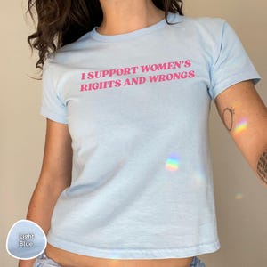 May include: Light blue t-shirt with the text "I SUPPORT WOMEN'S RIGHTS AND WRONGS" in pink. The shirt is a crew neck style and made of a soft material. The shirt is a light blue color.