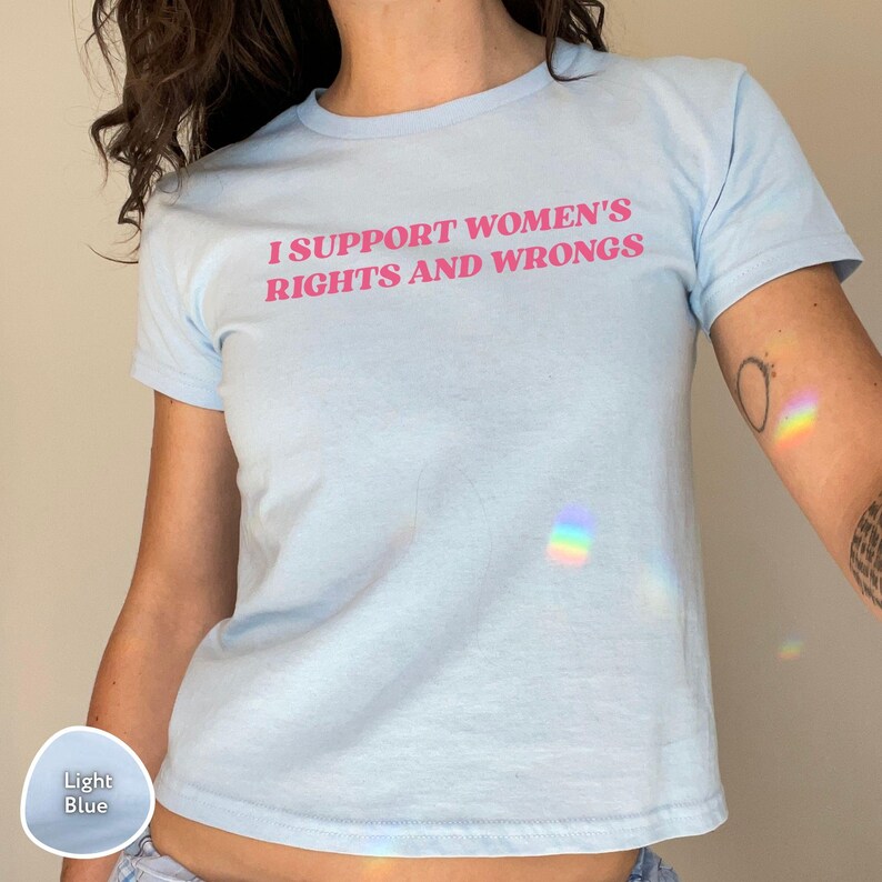 May include: Light blue t-shirt with the text "I SUPPORT WOMEN'S RIGHTS AND WRONGS" in pink. The shirt is a crew neck style and made of a soft material. The shirt is a light blue color.