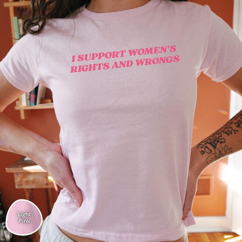 May include: Light pink t-shirt with the text "I SUPPORT WOMEN'S RIGHTS AND WRONGS" in bright pink lettering. The shirt is made of a soft material and has short sleeves. The person is wearing the shirt.
