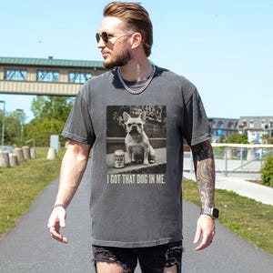 K&ouml;nnte beinhalten: Dunkelgraues T-Shirt mit einem Schwarz-Wei&szlig;-Bild einer franz&ouml;sischen Bulldogge mit Zigarette und einer Dose Urban Paw. Der Text "I GOT THAT DOG IN ME" steht darunter. Das T-Shirt wird von einer Person getragen.