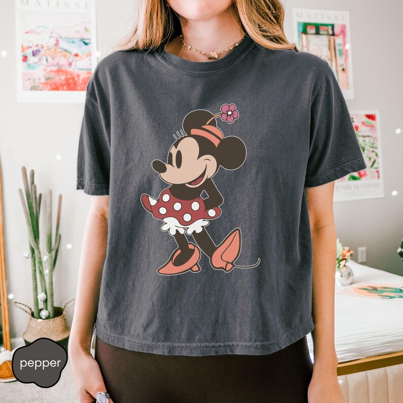 Op de afbeelding: Donkergrijs T-shirt met een cartoon illustratie van Minnie Mouse. Minnie Mouse draagt een rood-witte polkadot jurk, roze schoenen en een roze hoed met een bloem. Het T-shirt heeft een losse pasvorm.