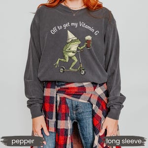 May include: Pepper-colored long-sleeve shirt with a graphic of a frog riding a scooter and holding a beer. The text "Off to get my Vitamin G" is printed above the frog. The shirt is made of a soft material.
