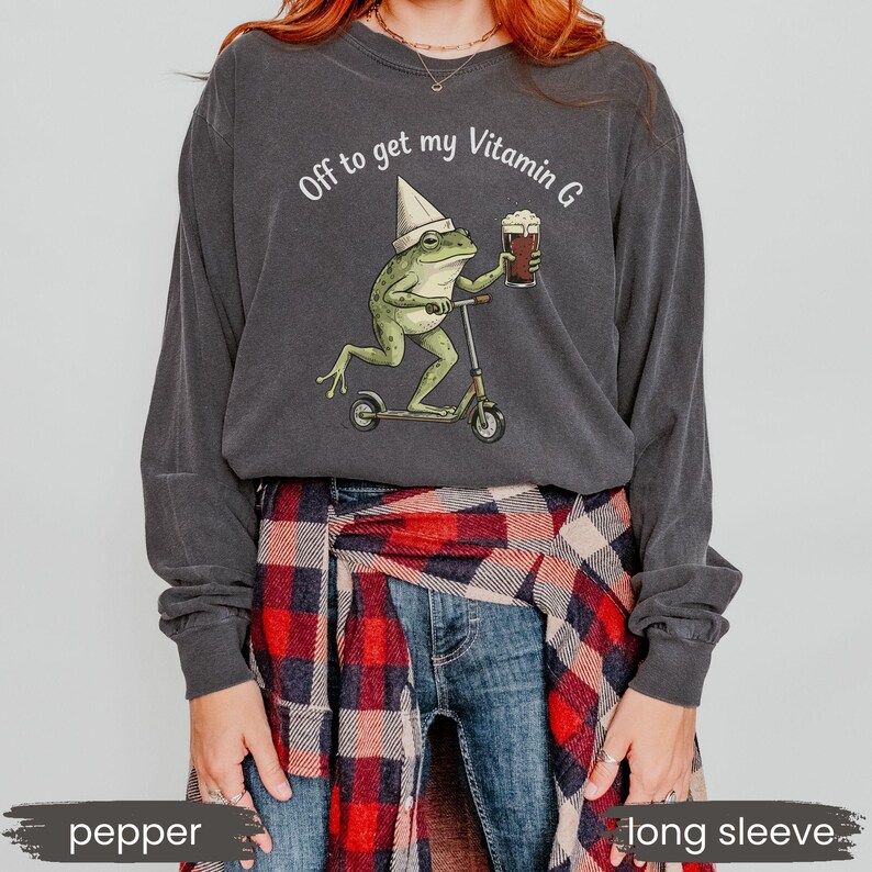 May include: Pepper-colored long-sleeve shirt with a graphic of a frog riding a scooter and holding a beer. The text "Off to get my Vitamin G" is printed above the frog. The shirt is made of a soft material.