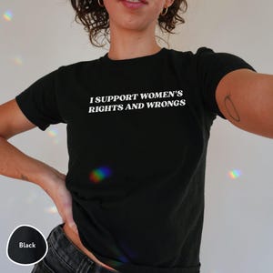 May include: Black crew neck t-shirt with the text "I SUPPORT WOMEN'S RIGHTS AND WRONGS" in white. The shirt is a solid black color and has short sleeves.