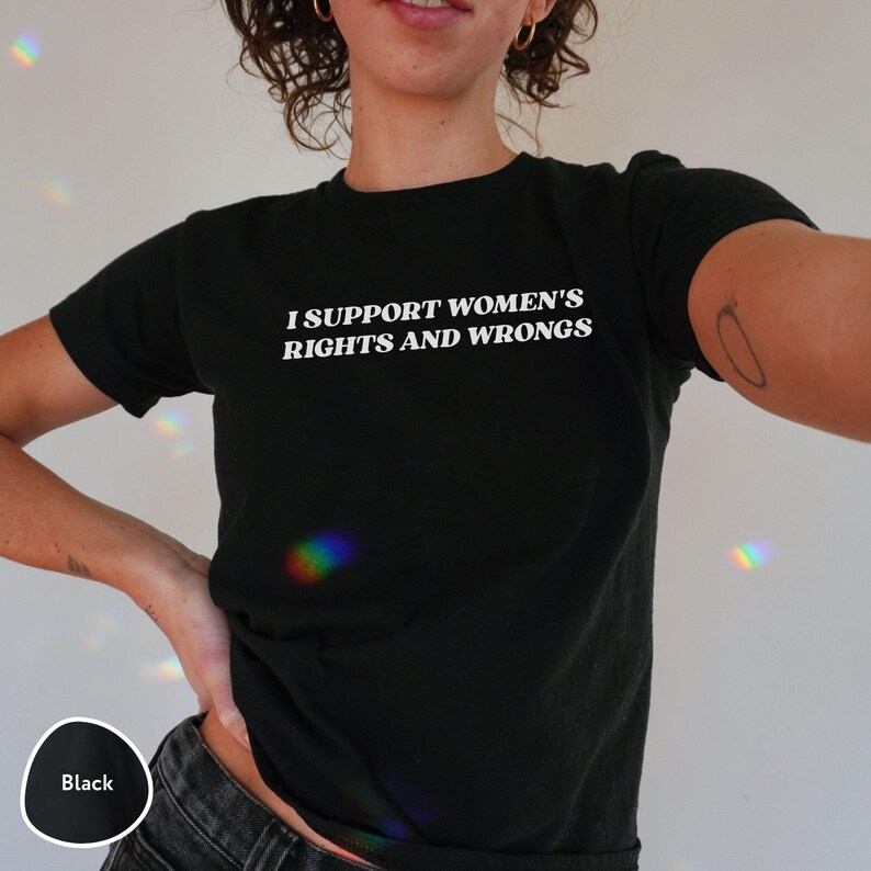 May include: Black crew neck t-shirt with the text "I SUPPORT WOMEN'S RIGHTS AND WRONGS" in white. The shirt is a solid black color and has short sleeves.