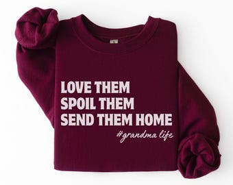 May include: A maroon sweatshirt with white text that reads "LOVE THEM, SPOIL THEM, SEND THEM HOME" and the hashtag "#grandma life". The sweatshirt is made of a soft material and has a crew neck.