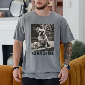 K&ouml;nnte beinhalten: Graues T-Shirt mit einem Schwarz-Wei&szlig;-Bild einer franz&ouml;sischen Bulldogge mit Zigarette im Mund, neben einer Dose "Urban Paw Lager". Der Text "I GOT THAT DOG IN ME" ist darunter gedruckt.