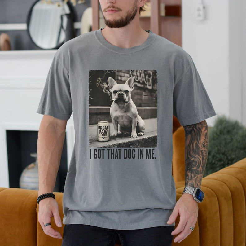 K&ouml;nnte beinhalten: Graues T-Shirt mit einem Schwarz-Wei&szlig;-Bild einer franz&ouml;sischen Bulldogge mit Zigarette im Mund, neben einer Dose "Urban Paw Lager". Der Text "I GOT THAT DOG IN ME" ist darunter gedruckt.