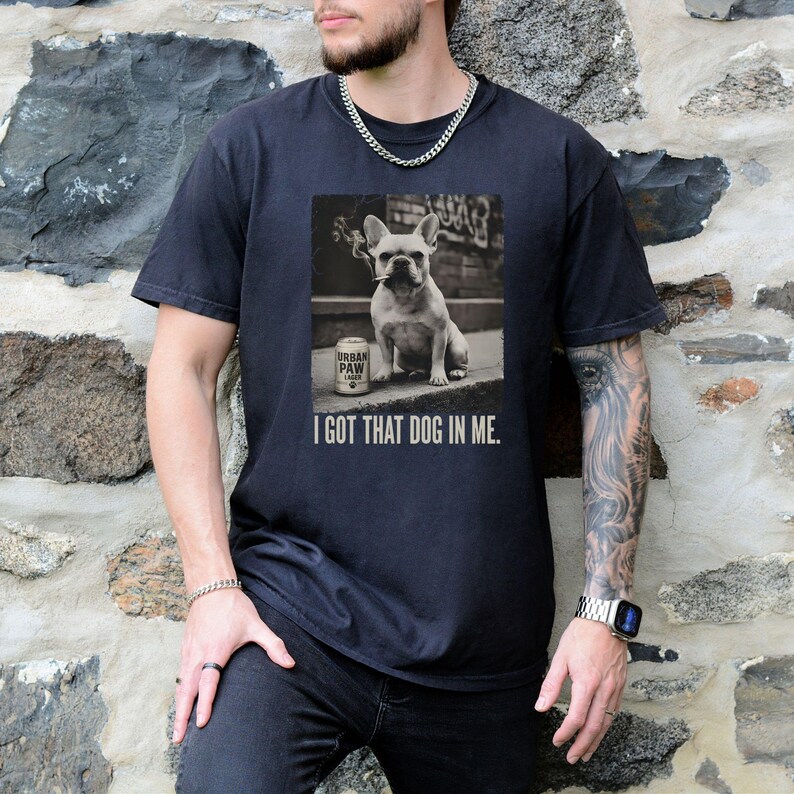 K&ouml;nnte beinhalten: Schwarzes T-Shirt mit einem Schwarz-Wei&szlig;-Bild einer franz&ouml;sischen Bulldogge mit Zigarette und einer Dose "Urban Paw Lager". Der Text "I GOT THAT DOG IN ME." steht darunter. L&auml;ssiger Stil.