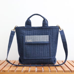 May include: A blue quilted tote bag with a gray pocket and a long adjustable strap. The bag has a small label that says "Littledoll".
