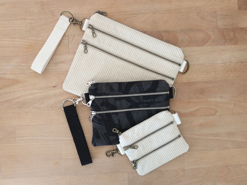 Mix and match your Wholecloth Pattern Tether Pouches. Shown here in 3 sizes, 2 bags are tan and cream stripe canvas with cream webbing wristlet, and one is black and gray printed canvas with silver hardware and a black cotton webbing wrist strap.