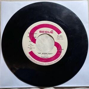 May include: A black vinyl record with a pink and white label. The label reads "SEGUE" at the top and features the song title "MR. MOONLIGHT" by Timothy. The record is a promotional copy and includes the WRS Recording Studios, Pittsburgh, Pennsylvania.