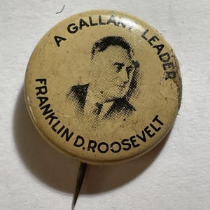 May include: Vintage pinback button with a portrait of Franklin D. Roosevelt. The button is circular, with the text "A GALLANT LEADER FRANKLIN D. ROOSEVELT" encircling the image. The button has a pin on the back.