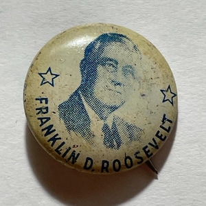 May include: Vintage campaign button featuring a portrait of Franklin D. Roosevelt in blue ink. The button has a cream-colored background with two blue stars and the text "FRANKLIN D. ROOSEVELT" in a circular arrangement.