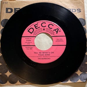 May include: A vintage black vinyl record with a pink label featuring the text "TELL ME WHAT'S ON YOUR MIND" by The Blendors. The record is in its original brown paper sleeve, with the Decca Records logo visible.