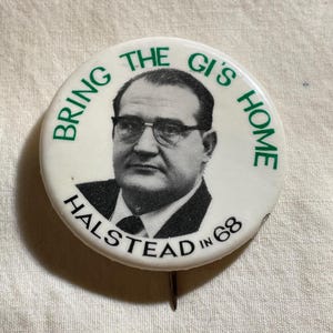 May include: A vintage white button with a black and white portrait of a man wearing glasses. The text "BRING THE GI'S HOME" and "HALSTEAD IN 68" are printed in green around the portrait. A pin is attached to the back.