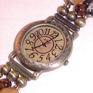 May include: A gold-toned wristwatch with a round face and Roman numeral hour markers. The watch is attached to a beaded bracelet with brown, black, and gold beads.