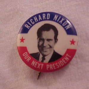 May include: A blue, white, and red button with a picture of Richard Nixon and the text "Richard Nixon Our Next President".