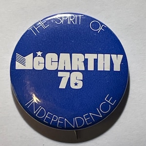 May include: A round, blue button with white text. The text reads "THE SPIRIT OF INDEPENDENCE" around the edge, with "McCARTHY 76" in the center. The button has a star graphic.