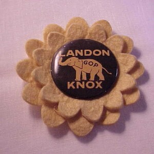 May include: A yellow flower-shaped button with a black and white button in the center. The button says "LANDON KNOX GOP" with an elephant graphic.