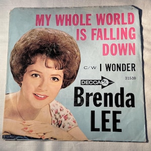 May include: Vintage vinyl record sleeve for Brenda Lee's song "My Whole World Is Falling Down." The cover features a portrait of Brenda Lee with text in pink and black on a light blue background. The record label is Decca.