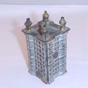 May include: A cast iron coin bank shaped like a building with a gray paint finish and gold accents. The bank has a slot on the top for coins and a door on the side to retrieve the coins.
