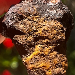 Può includere: Un esemplare minerale grezzo e irregolare caratterizzato da una sezione superiore cristallina, scura e metallica, che sfuma in una base strutturata di colore marrone terroso e ocra. La superficie presenta una topografia ruvida e frastagliata.