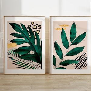 May include: Two framed prints with a tropical theme. The prints feature green leaves on a light pink background with gold and black accents.