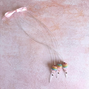 Puede incluir: Un conjunto de tres accesorios para el cabello en colores pastel. Cada accesorio presenta un pequeño diseño redondo con cuentas en tonos rosa, amarillo, azul y verde, con un extremo transparente y puntiagudo. Se adjuntan a alambres finos y una cinta rosa.