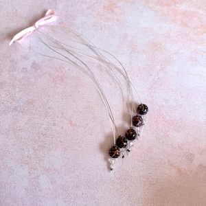 Puede incluir: Un conjunto de seis accesorios para el cabello con cuentas. Cada accesorio presenta una cuenta con estampado de leopardo marrón oscuro y negro, cuentas de cristal transparente y un alambre fino. Una cinta rosa está unida a los alambres.