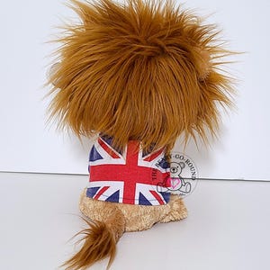 May include: A plush lion toy with a brown mane and tail, wearing a Union Jack shirt. The toy is tan and brown, with a fluffy mane and tail. The shirt features the British flag design.