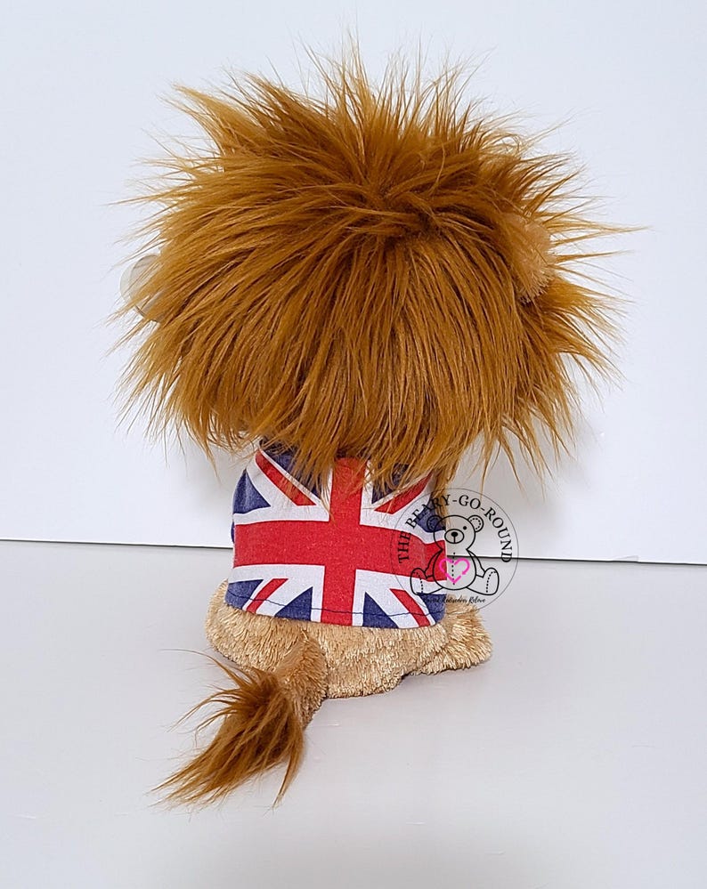 May include: A plush lion toy with a brown mane and tail, wearing a Union Jack shirt. The toy is tan and brown, with a fluffy mane and tail. The shirt features the British flag design.