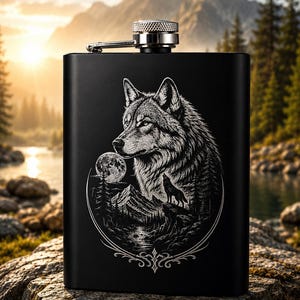 May include: A matte black metal flask featuring a detailed white laser-engraved illustration of a wolf head, a smaller wolf howling on a mountain cliff, a full moon, and a forest landscape, topped with a silver-toned screw-top cap.