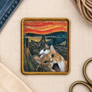 May include: A rectangular fabric patch featuring a printed parody of The Scream painting, replacing the central figure with two cats. The background displays a swirling orange sky and dark blue landscape. The patch has a thick, stitched gold border.