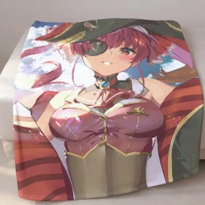 May include: A soft blanket with a colourful anime-style illustration of a character in a pirate-themed outfit. The character has red hair, an eye patch, and a maroon and gold outfit. The background shows a sky with clouds.