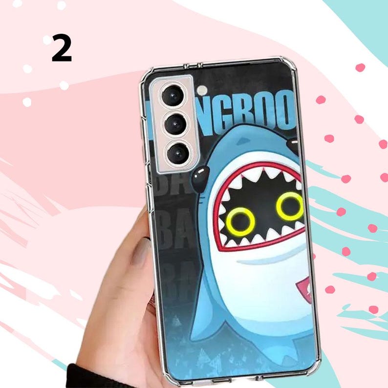 Puede incluir: Funda transparente para tel&eacute;fono con un dise&ntilde;o de tibur&oacute;n de dibujos animados, boca abierta y ojos amarillos. La funda tiene un fondo negro y azul con la palabra "NGROO" en azul. La funda est&aacute; dise&ntilde;ada para un tel&eacute;fono Samsung Galaxy.
