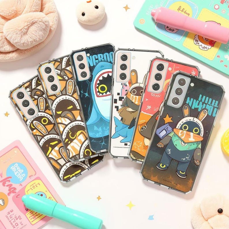 Puede incluir: Una colecci&oacute;n de fundas transparentes para tel&eacute;fonos con varios dise&ntilde;os de dibujos animados. Las fundas presentan im&aacute;genes de un tibur&oacute;n, un conejo y otros personajes en tonos azules, naranjas y marrones. Las fundas est&aacute;n dise&ntilde;adas para un smartphone.