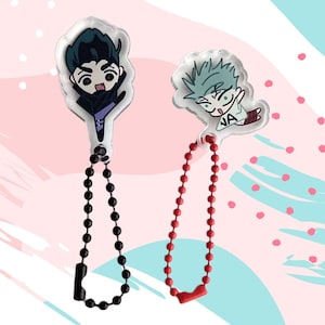May include: Two anime-style acrylic keychains. One features a character with dark hair and a black outfit, attached to a black beaded chain. The other keychain has a character with spiky, light blue hair, connected to a red beaded chain.