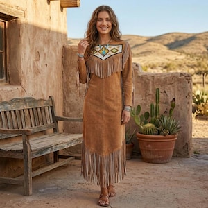 May include: A long, brown suede dress with fringe detailing. The dress has a decorative yoke with turquoise and white accents. The sleeves and hem are adorned with fringe. The woman is wearing sandals and jewellery.
