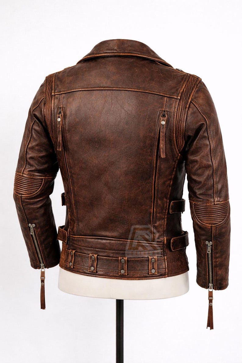 May include: A brown leather jacket with a distressed finish. The jacket features a notched collar, multiple zippered pockets, and ribbed detailing on the shoulders and elbows. It has a belt at the waist and a zipper closure. The jacket is displayed on a mannequin.